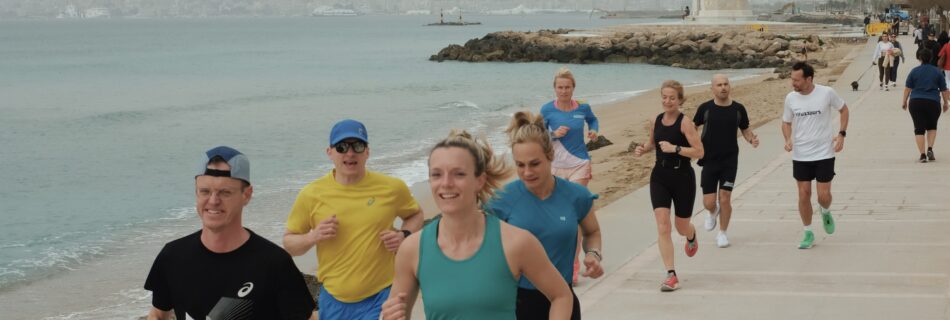 Runners jogging and smiling along the scenic Portitxol promenade in Palma, with views of the sea and harbor.